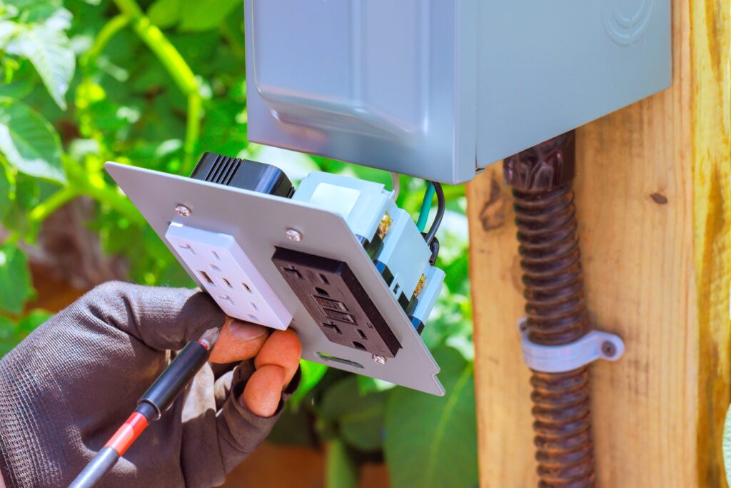 Electrician worker connects an outdoor outlet, USB ports to provide electrical access in garden setting.