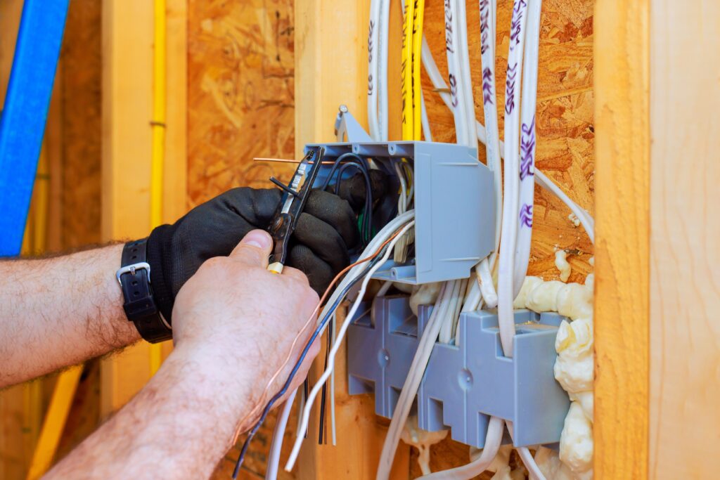 An electrician connects wires in wall box while wearing gloves at construction site